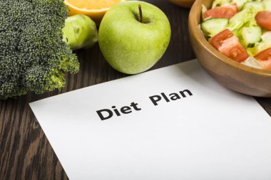 Gıda ve koyu ahşap bir masa üzerinde bir diyet planı ile kağıt.