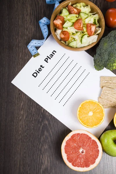 Food and sheet of paper with a diet plan on a dark wooden table. — Stock Photo, Image