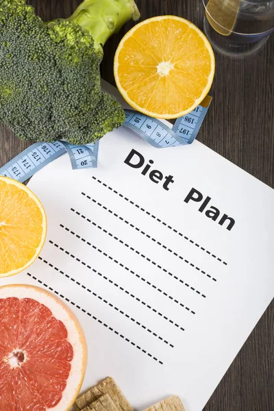 Food and sheet of paper with a diet plan on a dark wooden table. — Stock Photo, Image