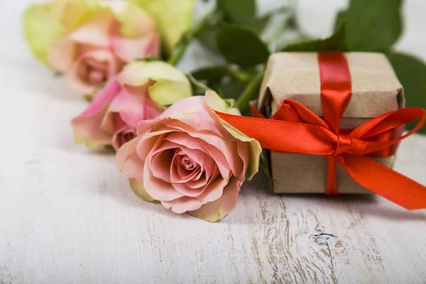 Růžové růže a dar na dřevěné pozadí. — Stock fotografie