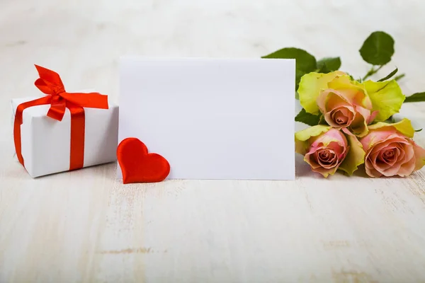 Rosa rosas, cartão, presente e corações em um fundo de madeira . — Fotografia de Stock