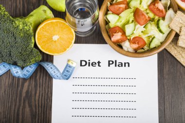 Gıda ve koyu ahşap bir masa üzerinde bir diyet planı ile kağıt.