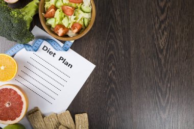 Gıda ve koyu ahşap bir masa üzerinde bir diyet planı ile kağıt.
