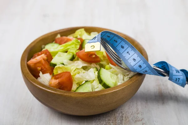 Salad in wooden bowl, fork and measuring tape on a table close-u — Stock Photo, Image