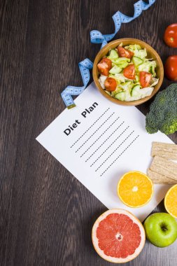 Gıda ve koyu ahşap bir masa üzerinde bir diyet planı ile kağıt.