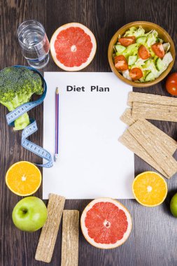 Gıda ve koyu ahşap bir masa üzerinde bir diyet planı ile kağıt.