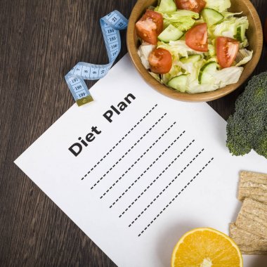 Gıda ve koyu ahşap bir masa üzerinde bir diyet planı ile kağıt.
