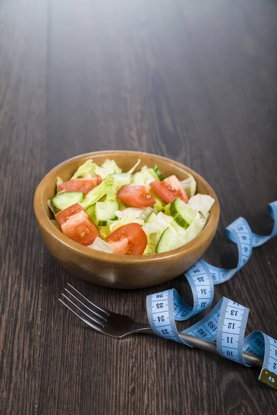Salad in wooden bow,forkl and measuring tape on a table close-up — Stock Photo, Image