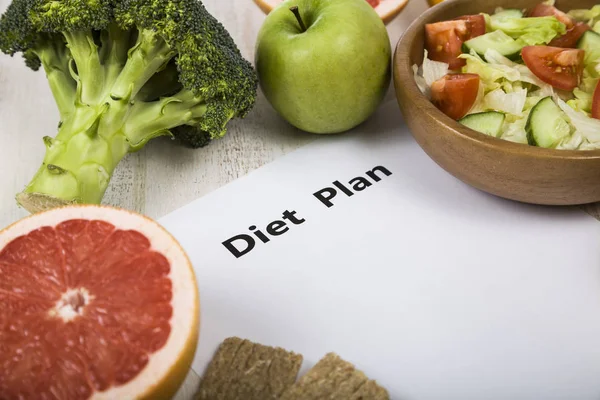 Voedsel en vel papier met een dieetplan op een houten tafel. — Stockfoto