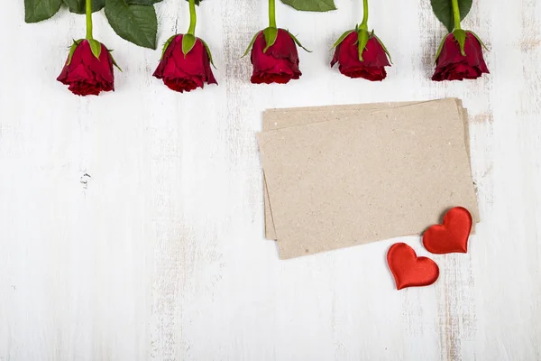 Las rosas rojas y el papel para las felicitaciones al fondo de madera . —  Fotos de Stock