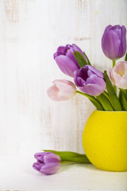 Ahşap arka plan üzerinde sarı bir vazoda Lale buketi. 
