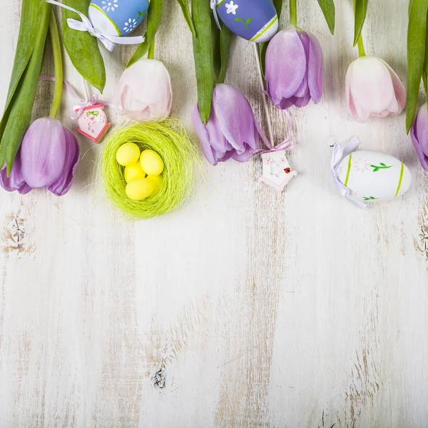 Fioletowe tulipany bukiet i pisanki na lekki drewniany stół. — Zdjęcie stockowe