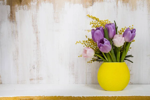 Ramo de tulipanes en un jarrón amarillo sobre un fondo de madera . — Foto de Stock