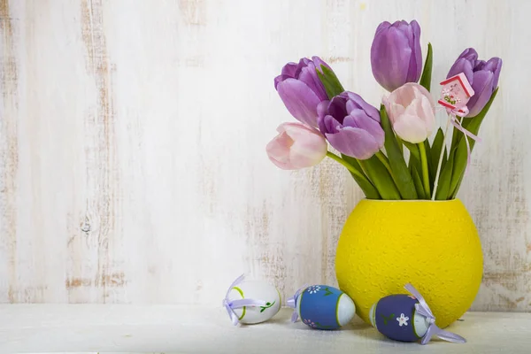 Букет фіолетових тюльпанів і великодніх яєць на легкому дерев'яному столі . — стокове фото