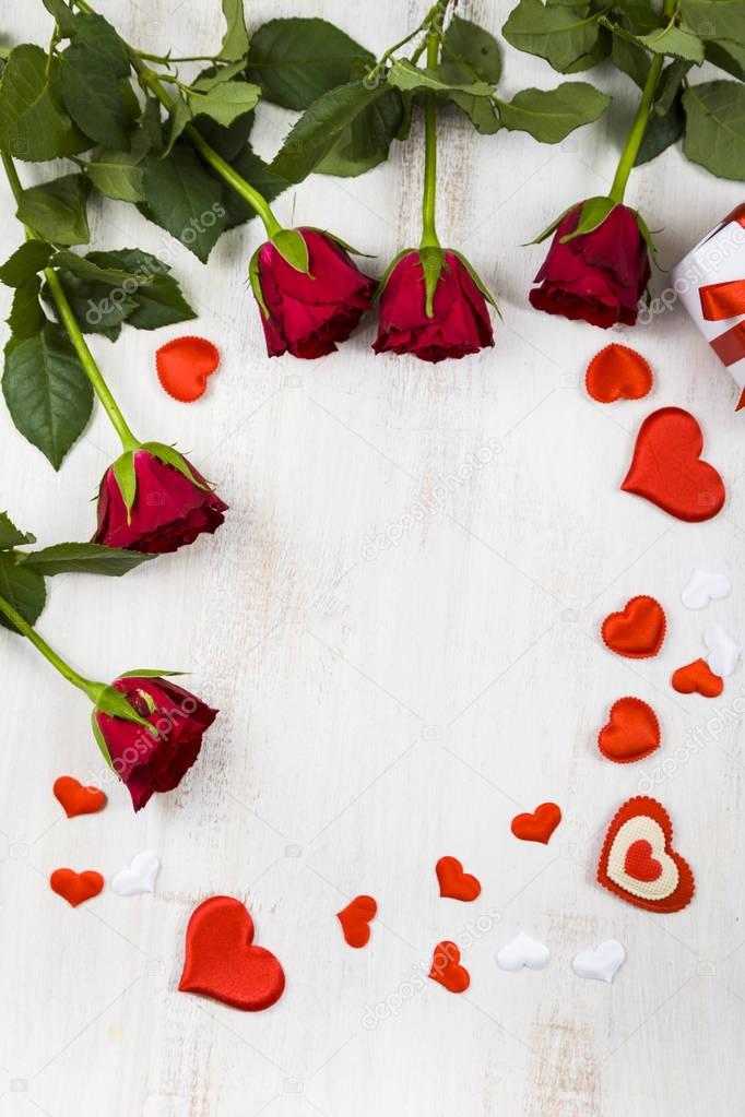 Frame of red roses and hearts on a wooden background. 