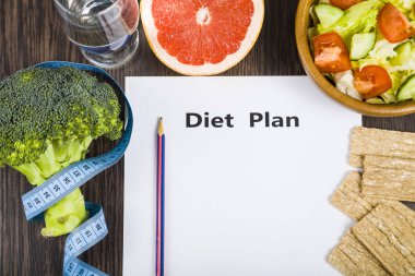 Gıda ve koyu ahşap bir masa üzerinde bir diyet planı ile kağıt.