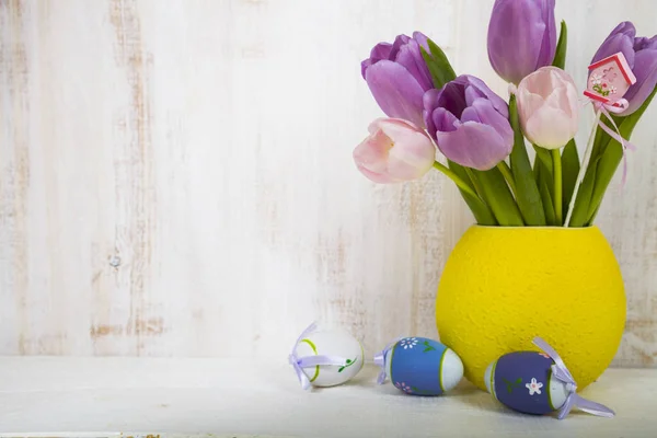 Bouquet purple tulips and Easter eggs on a light wooden table. — Stock Photo, Image