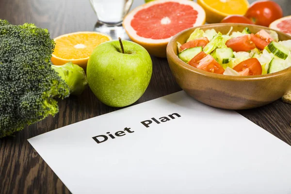 Food and sheet of paper with a diet plan on a dark wooden table. — Stock Photo, Image