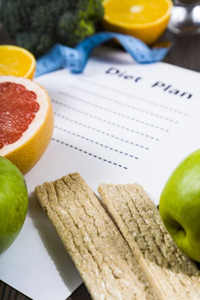 Food and sheet of paper with a diet plan on a dark wooden table.