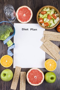 Gıda ve koyu ahşap bir masa üzerinde bir diyet planı ile kağıt.