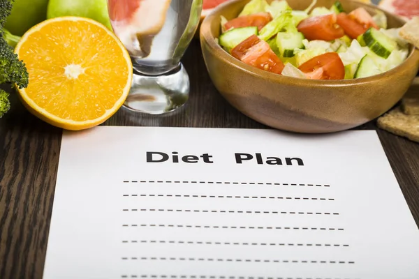 Food and sheet of paper with a diet plan on a dark wooden table. — Stock Photo, Image