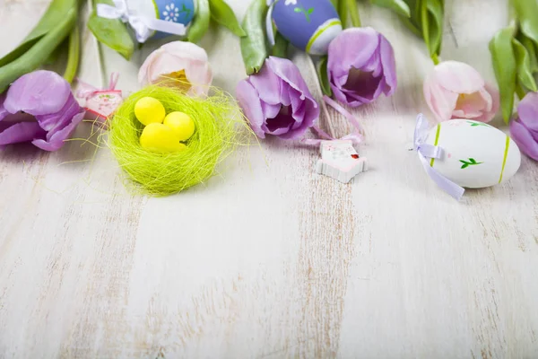 Fioletowe tulipany bukiet i pisanki na lekki drewniany stół. — Zdjęcie stockowe