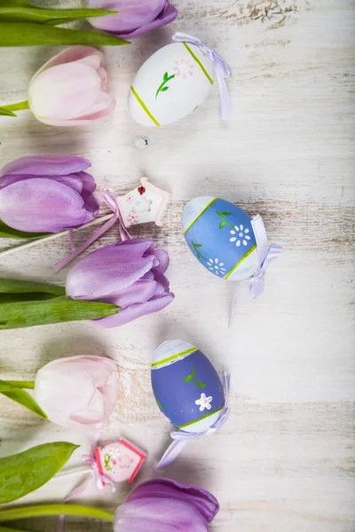 Ramo de tulipanes morados y huevos de Pascua en una mesa de madera clara . — Foto de Stock