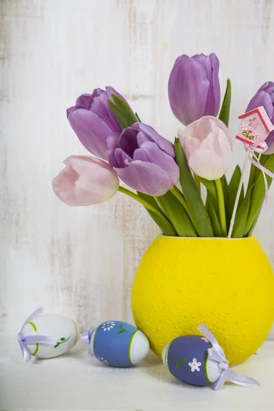 Bouquet purple tulips and Easter eggs on a light wooden table. — Stock Photo, Image