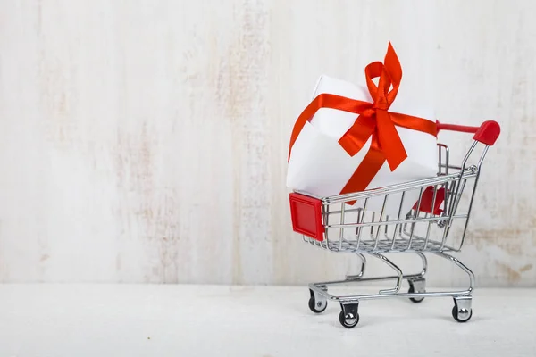 Shopping cart with gift box on a light wooden background.