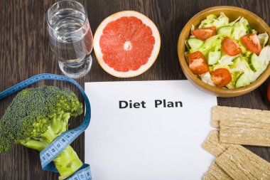 Gıda ve koyu ahşap bir masa üzerinde bir diyet planı ile kağıt.