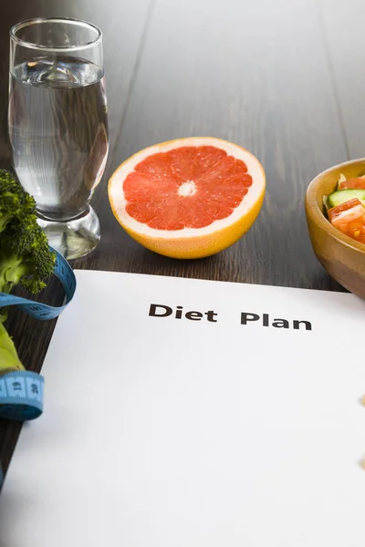 Food and sheet of paper with a diet plan on a dark wooden table. — Stock Photo, Image