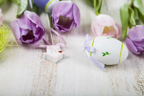 Bouquet purple tulips and Easter eggs on a light wooden table. — Stock Photo, Image