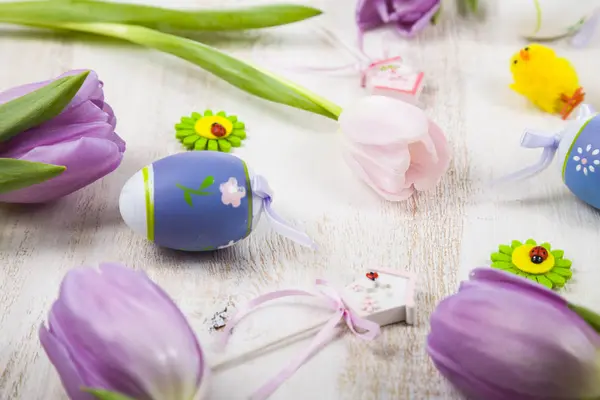 Bouquet purple tulips and Easter eggs on a light wooden table. — Stock Photo, Image