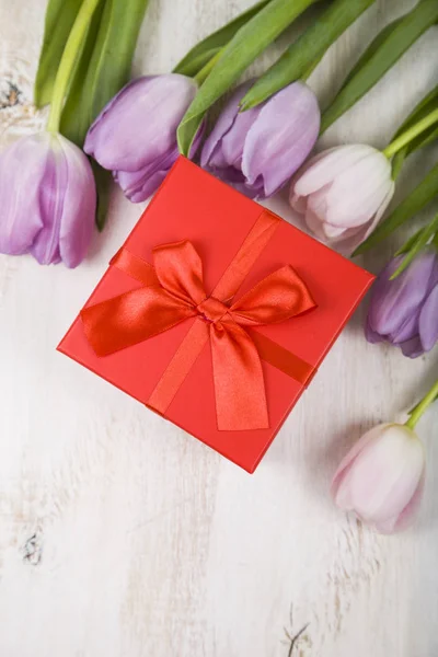 Bouquet de tulipes et un cadeau sur fond de bois . — Photo