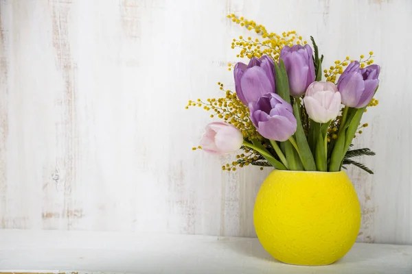 Bouquet of tulips and mimosa in a yellow vase on a wooden backgr — Stock Photo, Image