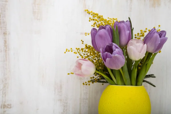 Ramo de tulipanes y mimosa en un jarrón amarillo sobre un fondo de madera — Foto de Stock