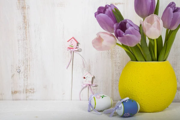 Bouquet purple tulips and Easter eggs on a light wooden table. — Stock Photo, Image