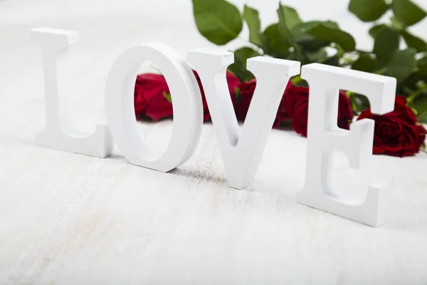 Κόκκινα τριαντάφυλλα, καρδιές και λέξη «αγάπη» σε φόντο ξύλινη. — Φωτογραφία Αρχείου