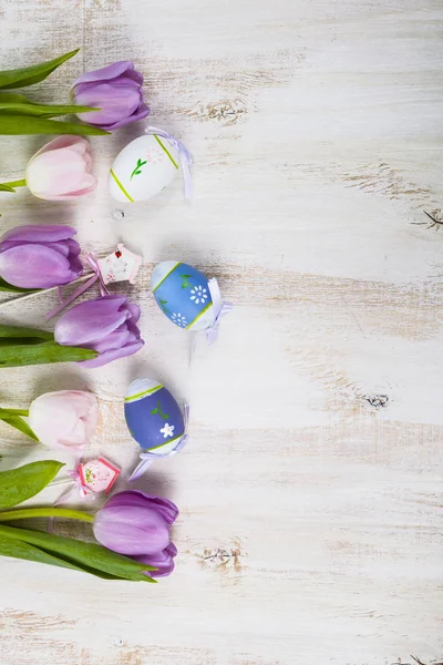Strauß lila Tulpen und Ostereier auf einem hellen Holztisch. — Stockfoto