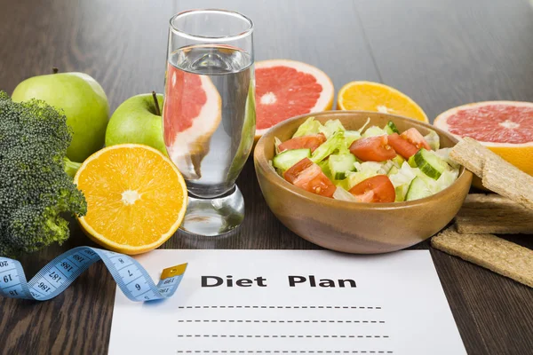 Comida e folha de papel com um plano de dieta em uma mesa de madeira escura . — Fotografia de Stock