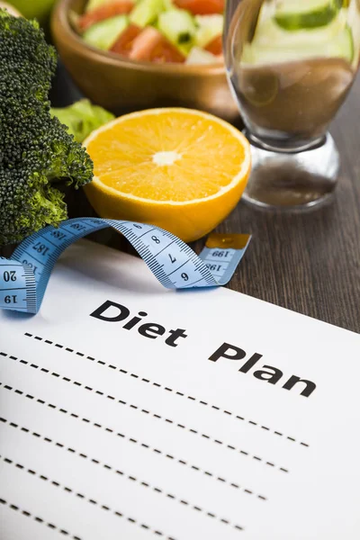 Food and sheet of paper with a diet plan on a dark wooden table. — Stock Photo, Image