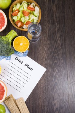 Gıda ve koyu ahşap bir masa üzerinde bir diyet planı ile kağıt.