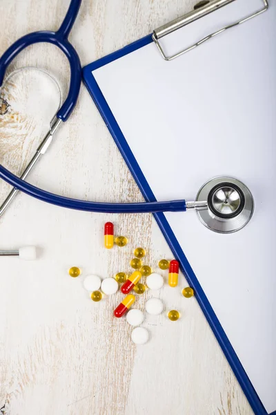 Comprimidos, comprimidos e estetoscópio à mesa de madeira . — Fotografia de Stock