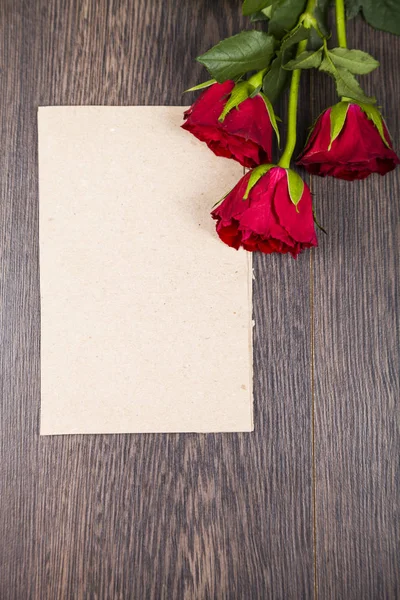 Red roses and card on a dark wooden background. — Stock Photo, Image