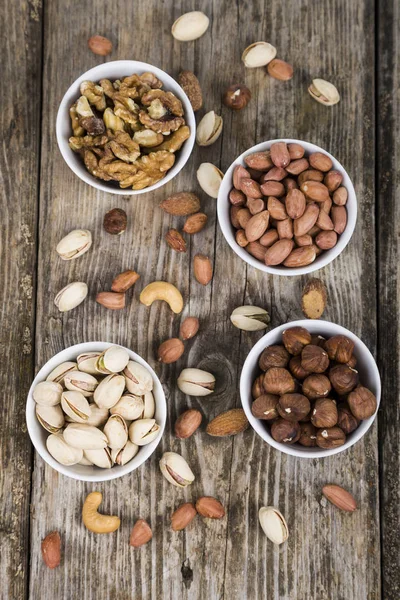 Cuatro cuencos con nueces en una mesa de madera — Foto de Stock