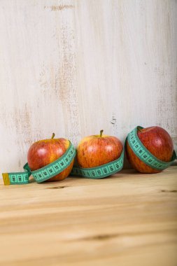 Üç elma ve ahşap bir masa üzerinde ölçüm bandı.  