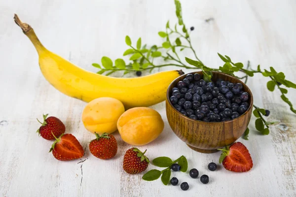 Mirtilos em uma tigela de madeira e frutas — Fotografia de Stock