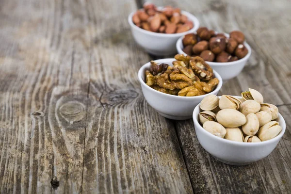 Cuatro cuencos con nueces en una mesa de madera — Foto de Stock