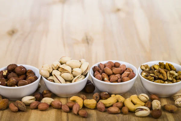 Cuatro cuencos con nueces en una mesa de madera — Foto de Stock