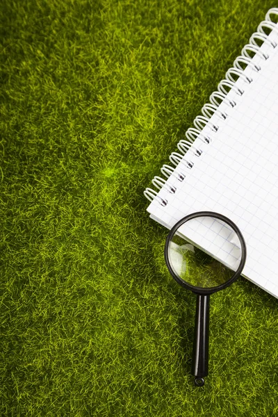 Notebook e lente d'ingrandimento sull'erba — Foto Stock